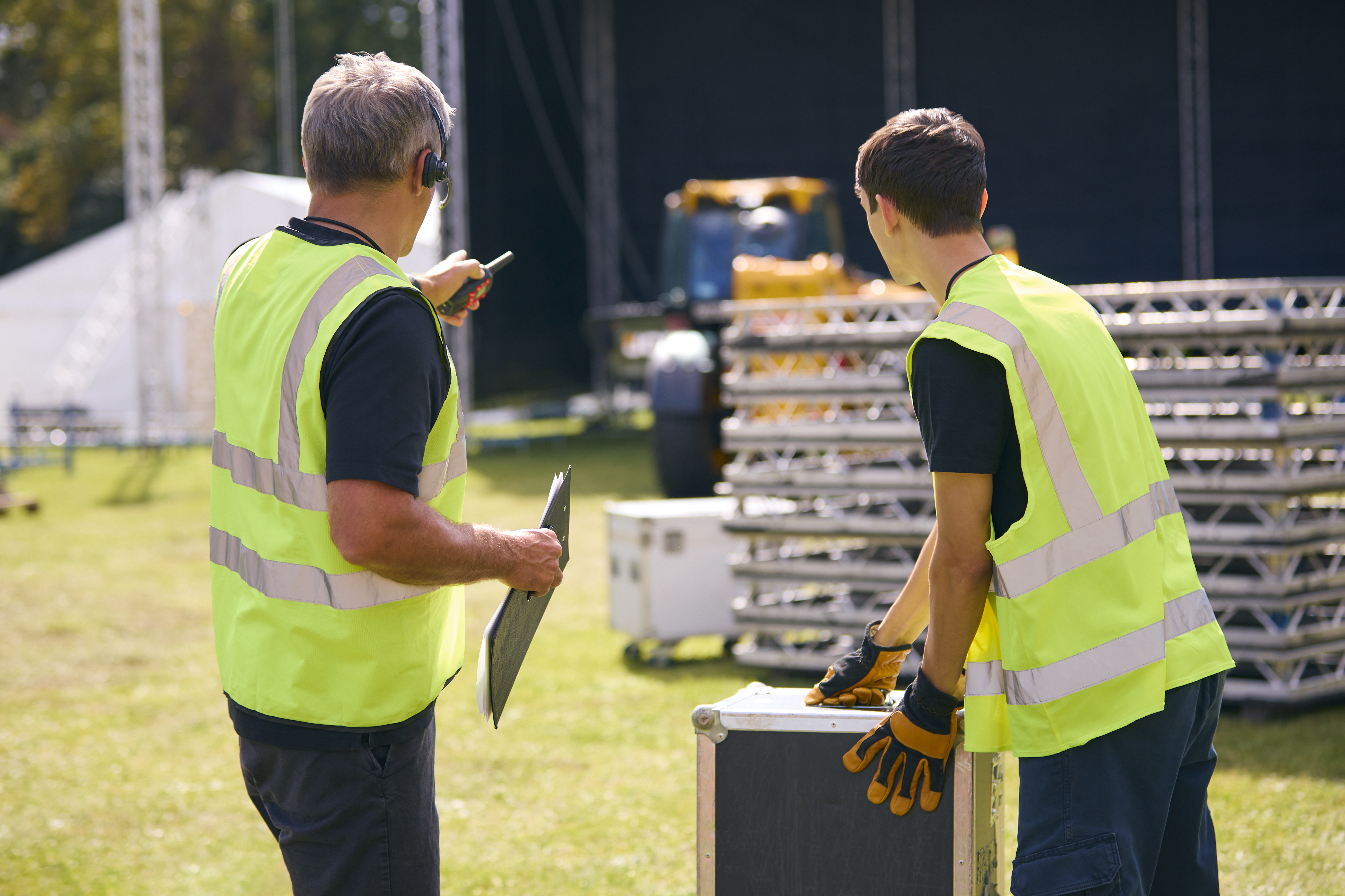 Male Production Team With Headsets Setting Up Outdoor Stage For Music Festival Or Concert
