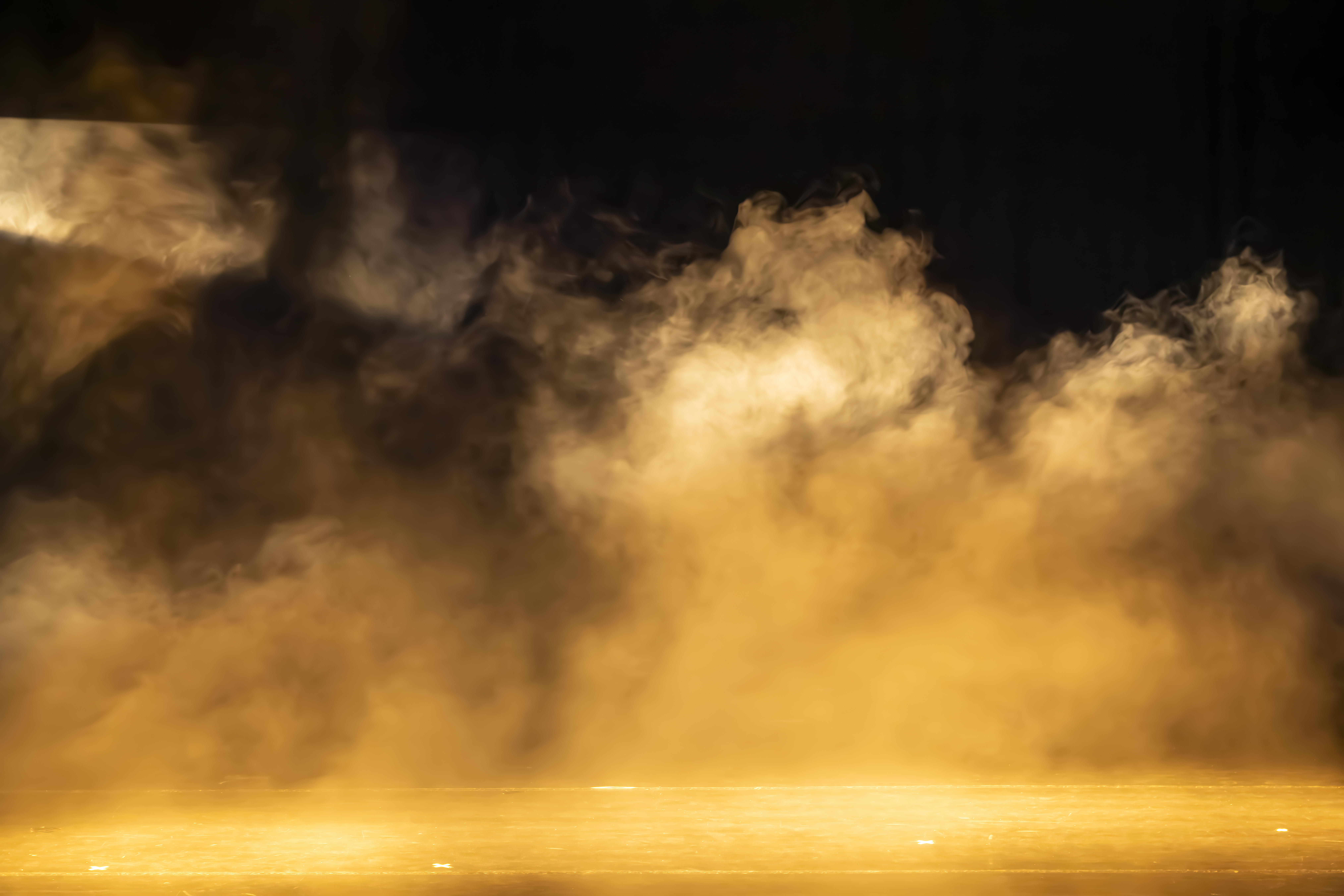 Smoke illuminated by golden light filling a dark stage, creating an atmospheric background