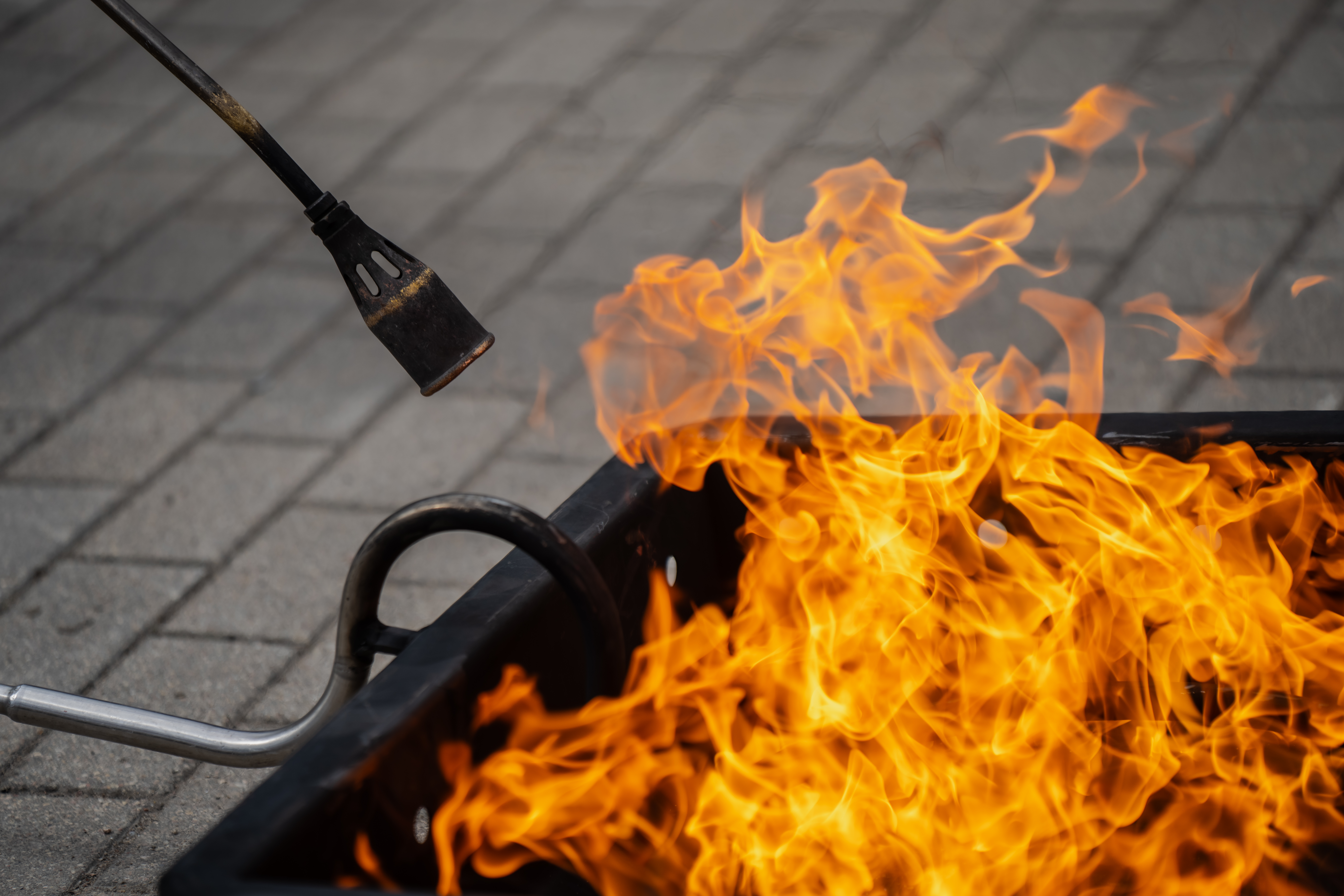Handheld gas torch burning bright orange flames inside a steel training tray for fire safety instruction and emergency response preparedness